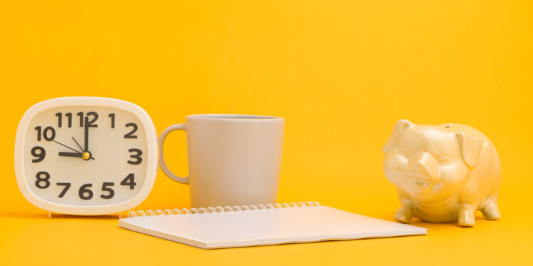 A white clock, a gray mug, a blank spiral notebook, and a white piggy bank are arranged on a bright yellow background—perfect for planning your short term savings goals. | Gyyol.com