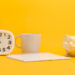 A white clock, a gray mug, a blank spiral notebook, and a white piggy bank are arranged on a bright yellow background—perfect for planning your short term savings goals. | Gyyol.com